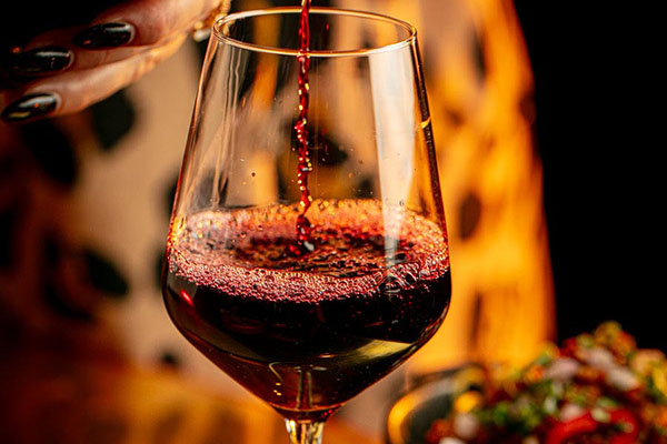 A person elegantly pouring red wine from a bottle into a glass
