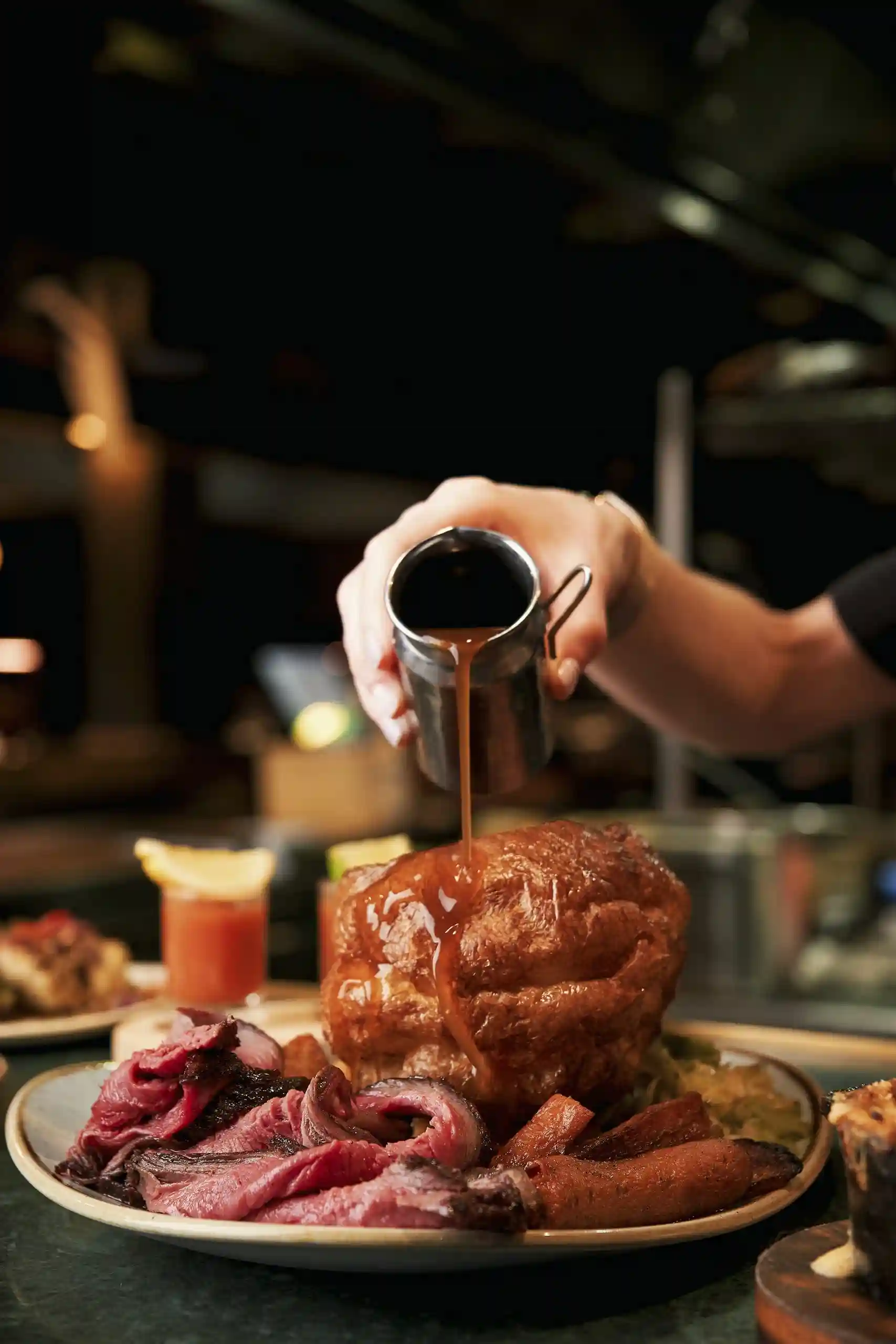 At Temper Restaurant, a person pours a drink over a plate of food, showcasing the steakhouse's vibrant dining experience