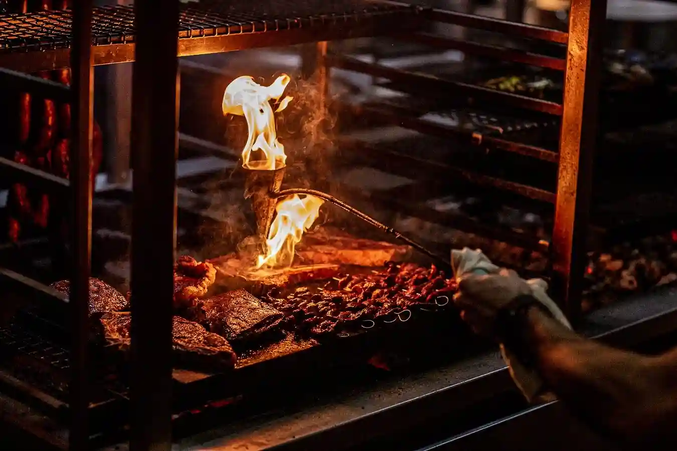 A man grills meat over flames at Temper, a London steakhouse known for fire-cooked steaks and barbecue dishes.