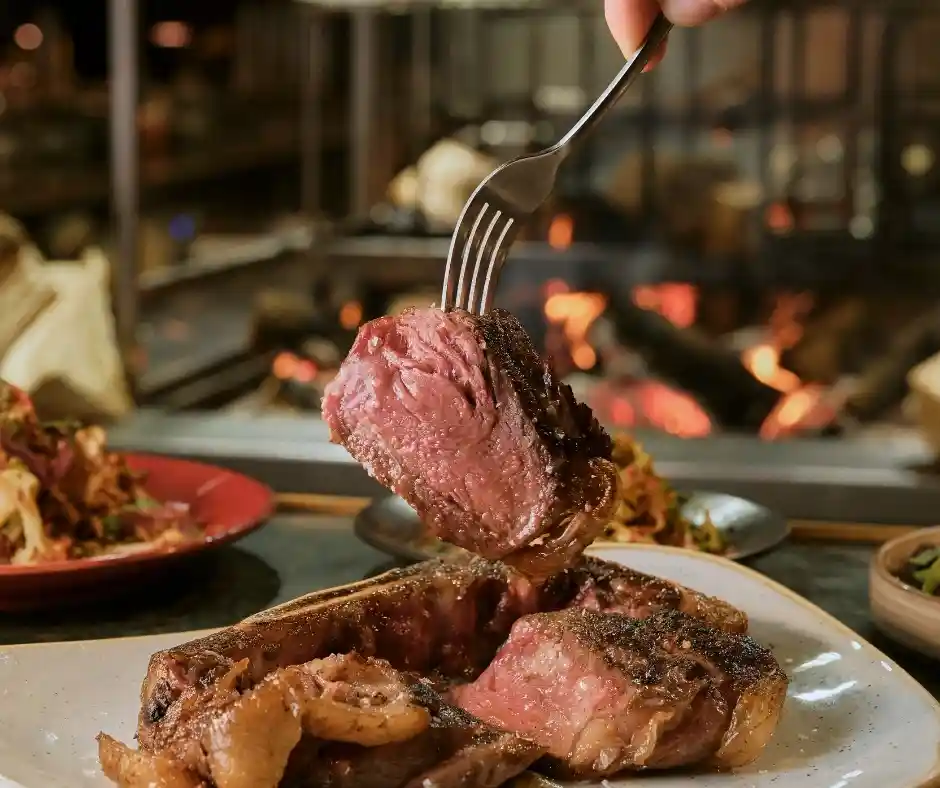 A diner holds a fork above a perfectly cooked steak on a plate at Temper Restaurant, known for its fire-cooked meats.