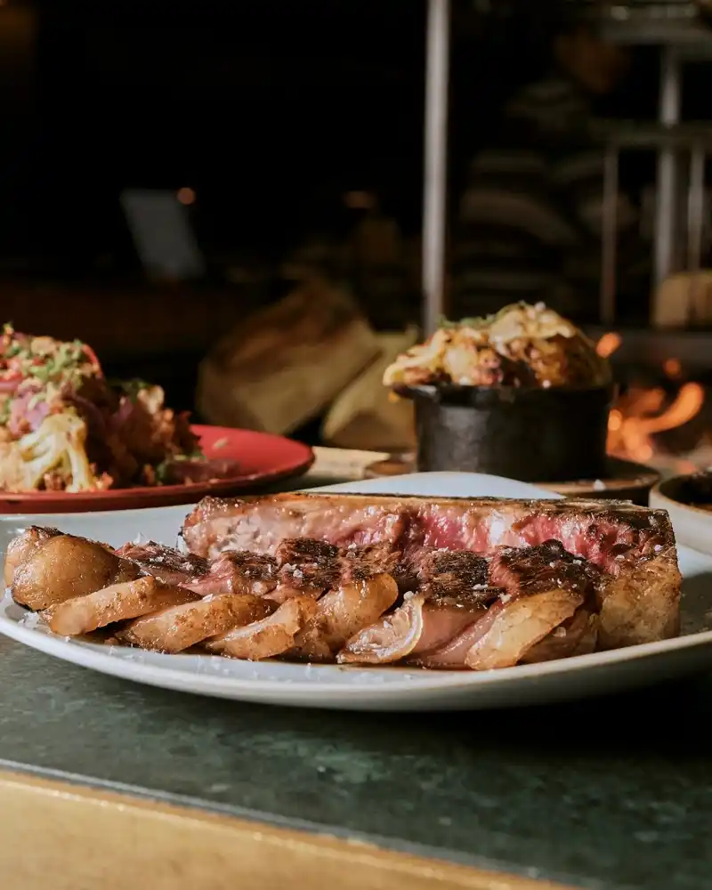 A beautifully arranged plate of steak and sides, with a fork and knife, set on a table at Temper Restaurant
