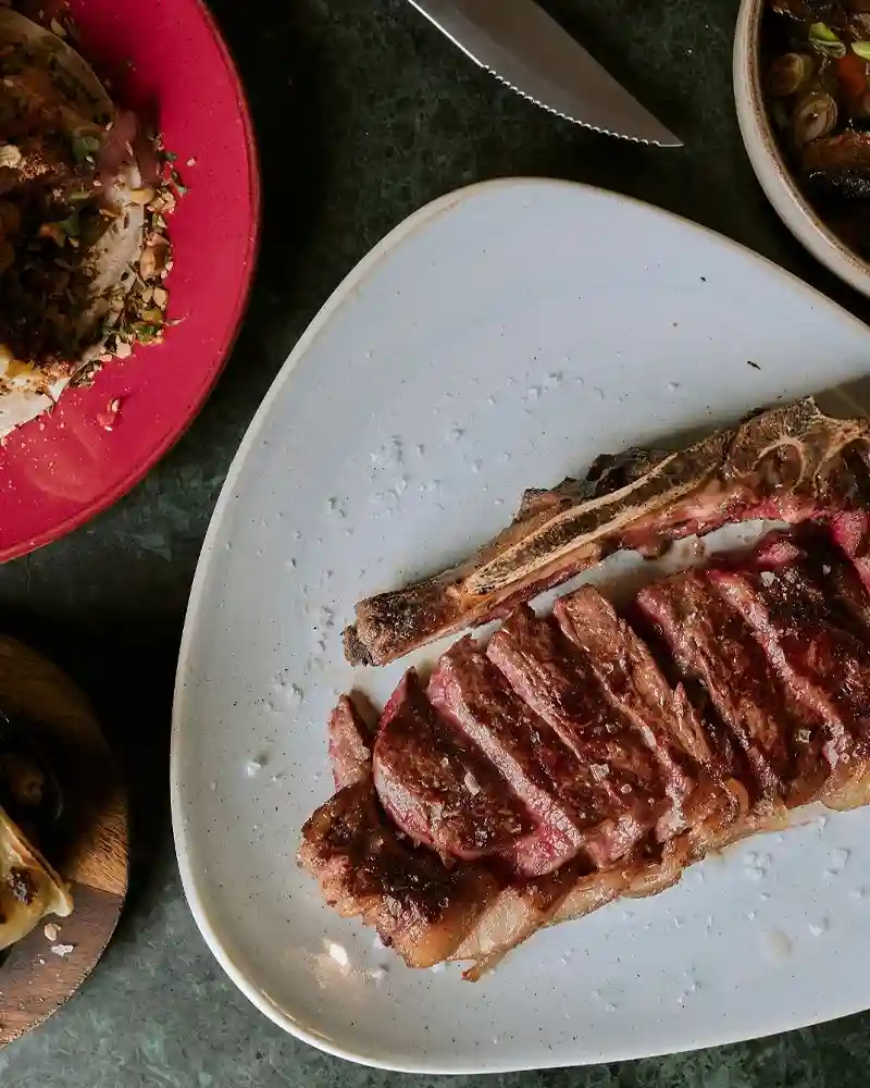 A perfectly cooked steak on a plate, accompanied by a knife and fork, showcasing a dish from Temper Restaurant in London.