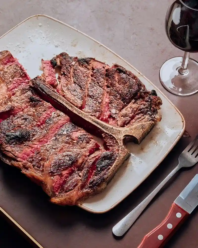 A perfectly cooked steak on a plate accompanied by a glass of red wine, showcasing a dining experience at Temper Restaurant