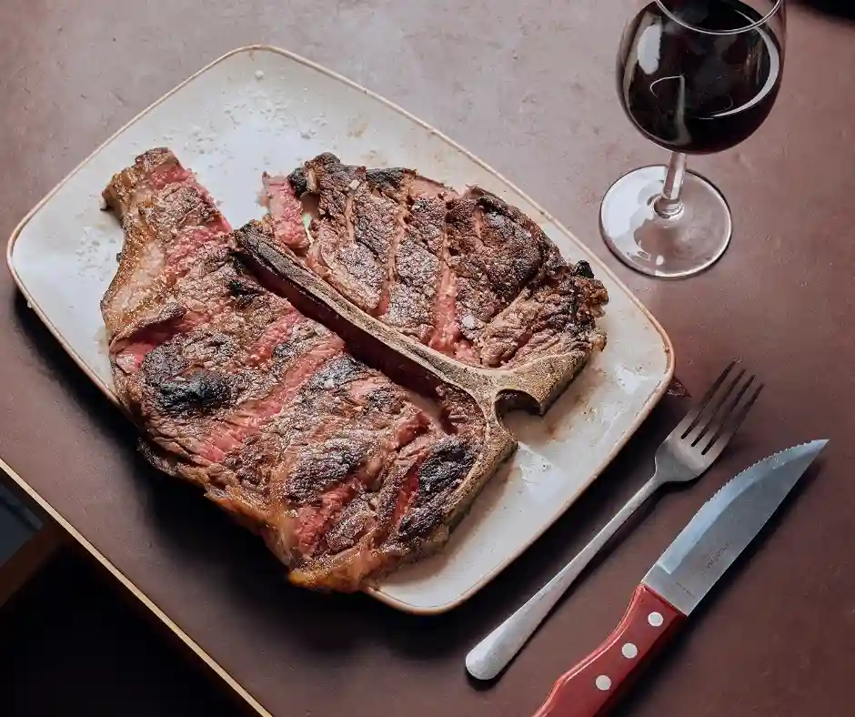 A perfectly cooked steak on a plate, accompanied by a knife and fork, showcasing a dish from Temper Restaurant in London