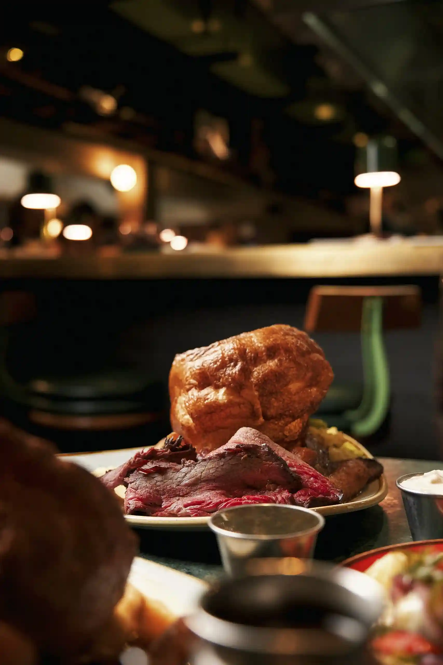 A table filled with a variety of dishes, showcasing steaks, smoked meats, and tacos from Temper Restaurant in London